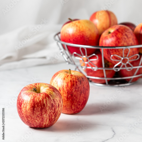 A bowl of fresh gala apples with two in front, against a light background.