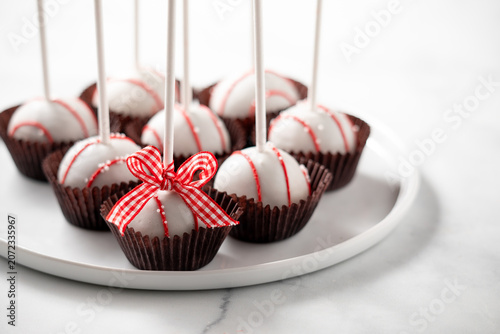 Decorated cake pops in paper liners on a rimmed plate against a light background