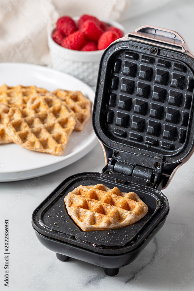Naklejka premium A freshly made heart shaped mini waffle on a mini waffle maker. 