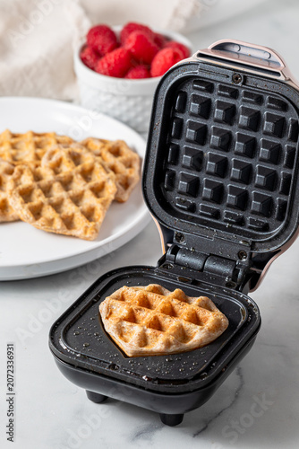A freshly made heart shaped mini waffle on a mini waffle maker. 