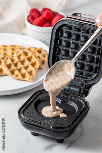 A spoon pouring waffle batter onto a mini waffle maker.