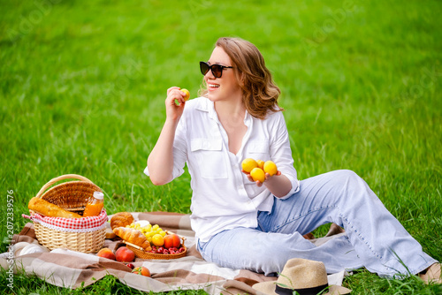 Cuadro en lienzo Cheerful woman with fresh apricot on picnic blanket in summer park