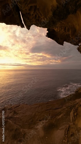 Slow motion fisheye video of sunrise over the ocean framed by a natural rock opening along the Sydney coastline, with calm water reflecting soft golden morning light, Australia.