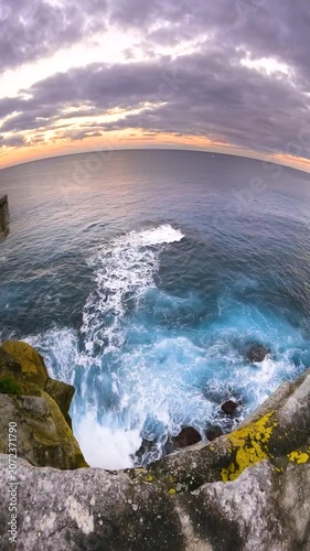 Slow motion fisheye video of Bondi Beach viewed from a coastal lookout at sunset, with calm ocean water, soft golden light, and the Sydney coastline, Australia.