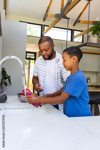 Vászonkép African American father and child rinsing purple vegetable under chrome faucet a