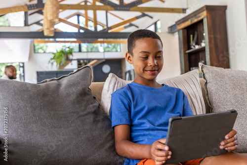 Vászonkép African American father and son sitting on gray sofa in living room, child holdi