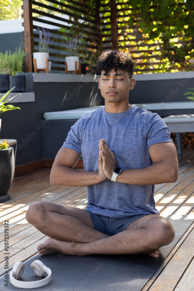 Obraz premium Male meditating with hands in prayer on yoga mat on wooden deck near headphones, smartwatch