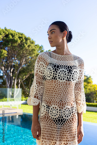 African woman standing poolside wearing cream crochet coverup over black bikini and gold hoops
