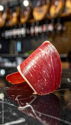 Thin slice of dry cured jamon iberico ham on dark marble, gourmet spanish food delicacy, tapas platter ingredient, high protein snack, luxury catering