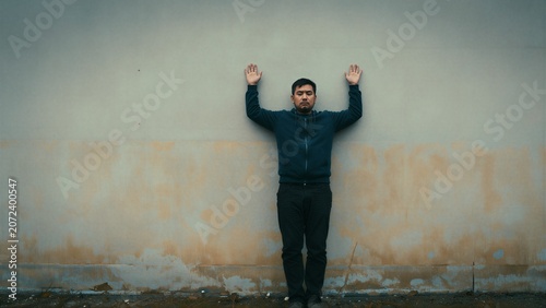 Man with Hands Raised in Surrender Against a Weathered Wall