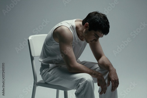 Depressed young man sitting alone on a chair in a minimalist studio