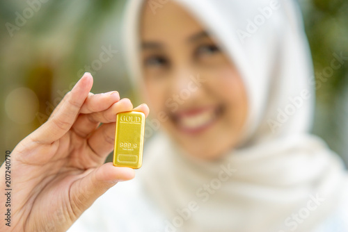 A young Asian Muslim woman is holding a gold bar. She looks very happy and joyful.