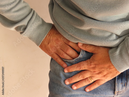 Closeup of man in blue sweater touching his hip in pain. Body pain concept.