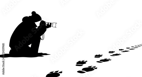 A silhouette of a photographer kneeling in the snow tracking animal footprints.