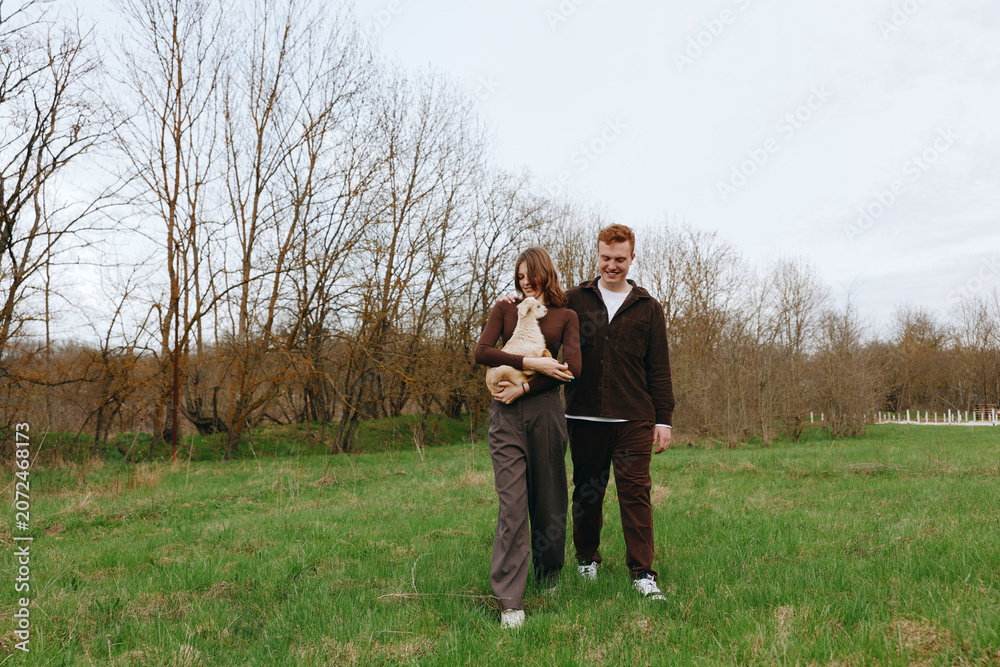 Obraz premium Outdoor family scene with a goat kid, a relaxed walk in a sunlit field, casual clothing, gentle breeze, natural colors, a candid moment of togetherness amid open nature