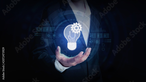 Innovation at Hand: A businessman holds a glowing lightbulb symbolizing innovation and new ideas, surrounded by futuristic digital graphics.