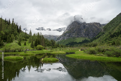 Natural Scenery of Valleys, Lakes, and Forests Beneath Snow-Capped Mountains Shrouded in Clouds and Mist