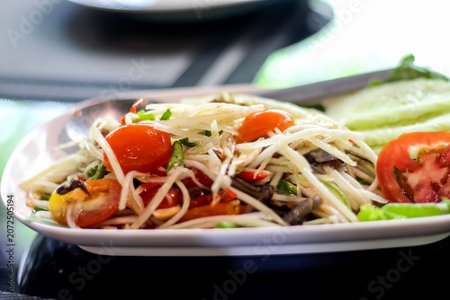 Close up spicy thai papaya salad  with salted crab and fermented fish on white plate table background