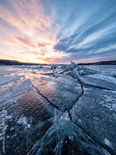 Frozen lake ice shards at sunset, cracked arctic winter landscape, dramatic sunrise over icy water, cold blue and orange nature scenery