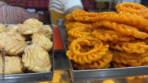 A vibrant street-side market display of traditional syrup-soaked sweets including intricate imarti, layered crispy khaja, and soft, aromatic malpua, West Bengal, India.