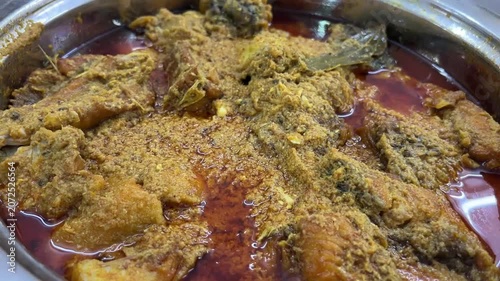 A traditional bowl of rich, aromatic Katla fish curry prepared in authentic Kolkata style with green chillies and a drizzle of pure mustard oil, West Bengal, India.