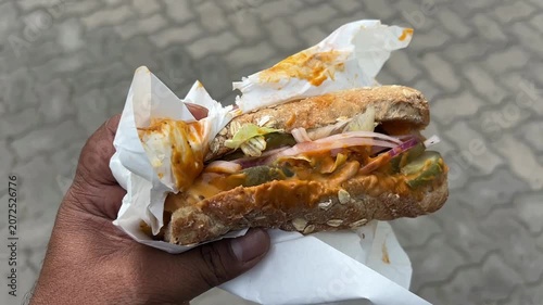 A detailed shot of a hand holding a delicious, toasted subway sub overflowing with fresh toppings and savory sauces, ideal for food delivery app banners.