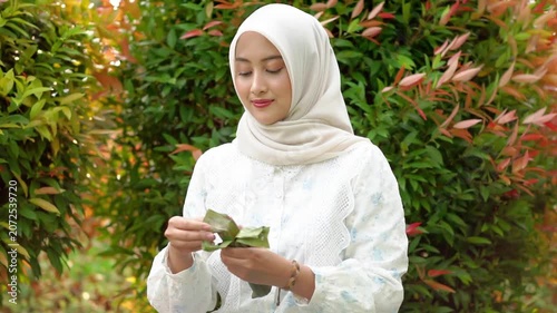 A young Asian Muslim woman is enjoying getuk pisang, a specialty food from Kediri, Indonesia, made from mashed steamed bananas wrapped in banana leaves.