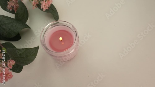 Burning candle and pink flowers on white table.