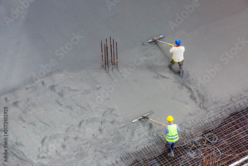 Obraz na plátně Construction workers flattening and smoothing fresh concrete on a monolithic bui