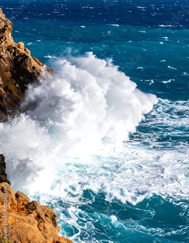 Powerful ocean wave crashing against rocky cliffside with white foam