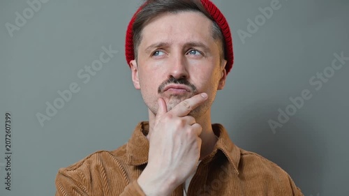 A man in a brown jacket and red beanie shows various thoughtful expressions while posing against a grey backdrop. He appears to be contemplating different ideas and emotions in each frame