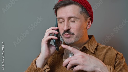 A young man is engaged in a phone conversation while holding a glass in one hand. He shows various expressions and gestures as he talks, creating a lively interaction