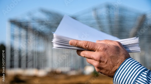 Hand holding documents against a blurred industrial framework