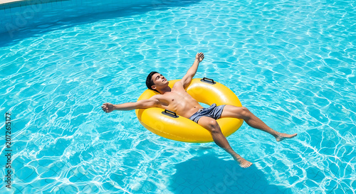 Carefree young man floating on yellow inflatable tube in blue crystal clear swimming pool water