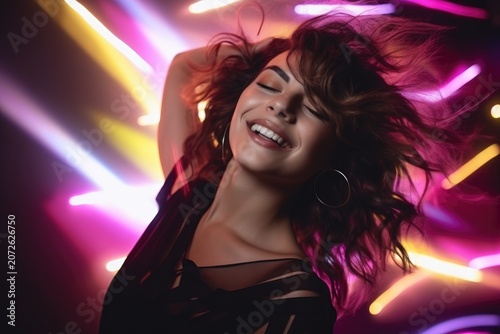 Smiling woman dancing with eyes closed under colorful neon light streaks, wearing hoop earring and black top