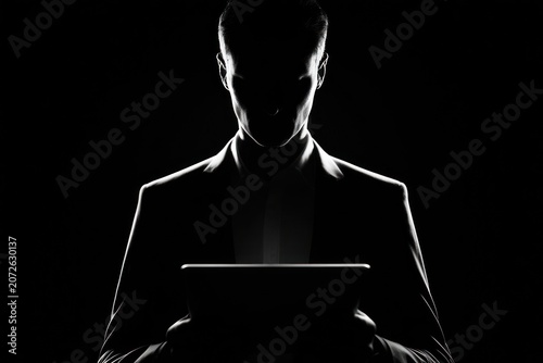 Silhouette of man holding tablet, dramatic lighting against black background