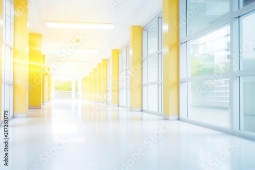 Bright empty corridor with yellow columns, glossy floor, and large windows with sunlight streaming in