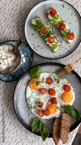 Healthy breakfast set with fried eggs, cherry tomatoes, avocado crispbreads and hot cocoa with marshmallows, top view.