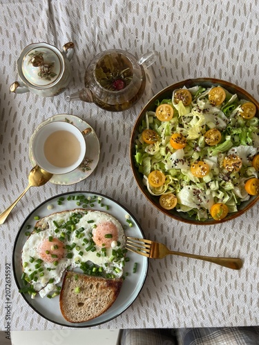 Healthy breakfast with fried eggs, green onions, fresh vegetable salad and herbal tea in a glass teapot, top view.