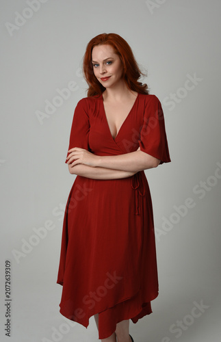 portrait of beautiful model with long red hair, wearing an elegant red vintage dress. standing pose,  isolated silhouette figure on studio background.