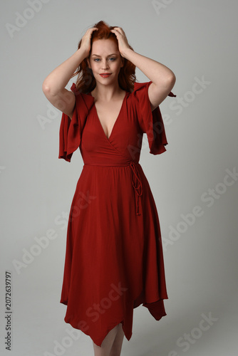 portrait of beautiful model with long red hair, wearing an elegant red vintage dress. standing pose,  isolated silhouette figure on studio background.