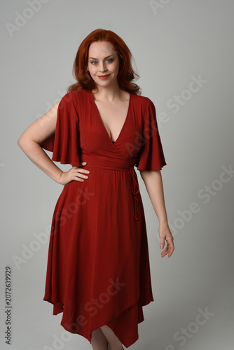 portrait of beautiful model with long red hair, wearing an elegant red vintage dress. standing pose,  isolated silhouette figure on studio background.