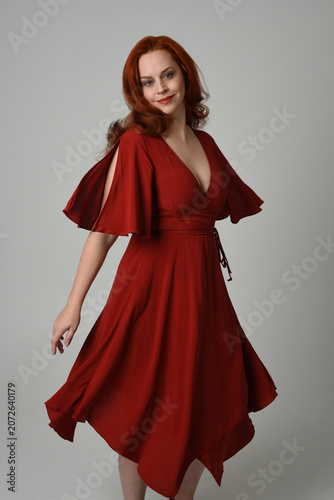 portrait of beautiful model with long red hair, wearing an elegant red vintage dress. standing pose,  isolated silhouette figure on studio background.
