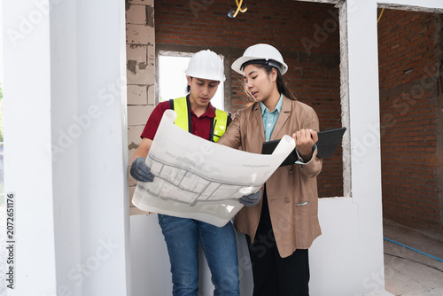 Asian engineer holding paper work and female architect reviewing architectural plans at a renovation or construction site