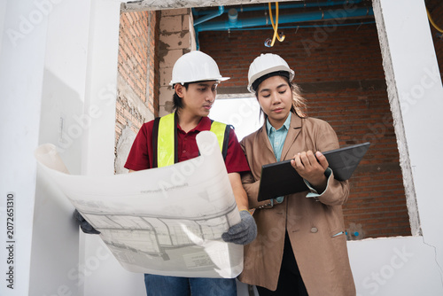 Asian engineer holding paper work and female architect reviewing architectural plans at a renovation or construction site