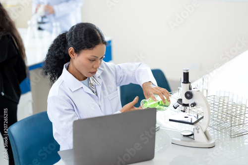 African American female scientist working with microscope and notebook computer in laboratory