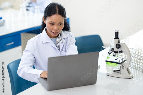 African American female scientist working with microscope and notebook computer in laboratory