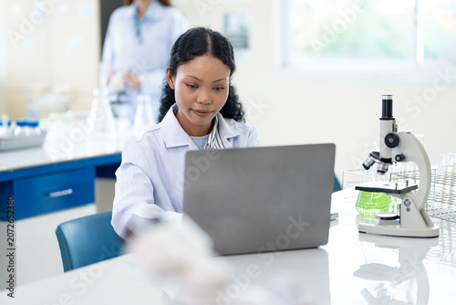 African American female scientist working with microscope and notebook computer in laboratory