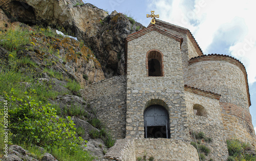 The church of the Elia Monastery at the foot of a cliff. The walls are light stone, the roof is tiled. Elia, Kakheti, Georgia