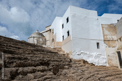 View of the Roman Theatre of Cádiz with surrounding historic buildings in Cádiz, Andalusia, Spain, showing ancient Roman ruins integrated into the urban architecture under a blue sky with clouds